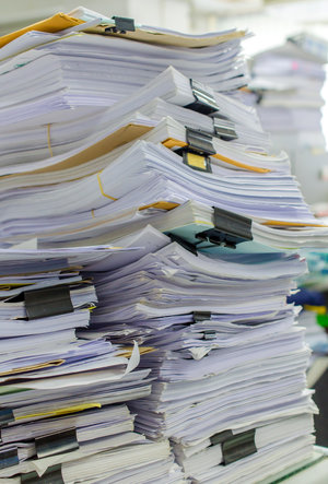 Pile of documents on desk stack up high waiting to be managed